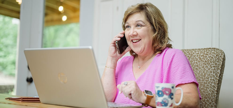 woman in a pink shirt on the phone with a laptop