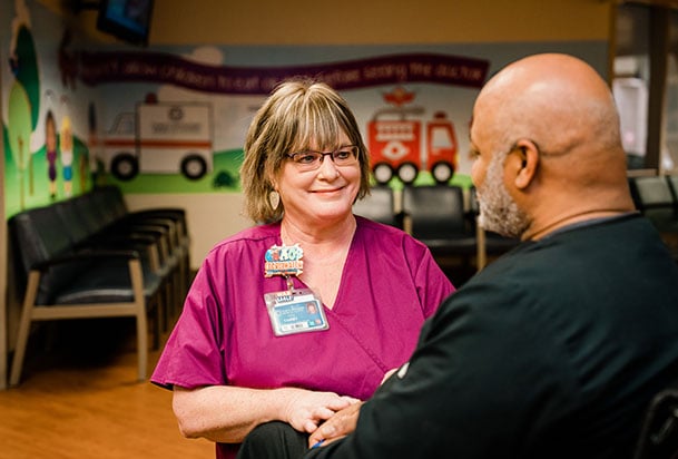 Nurse in pink scrubs holding a man's hand and talking with him