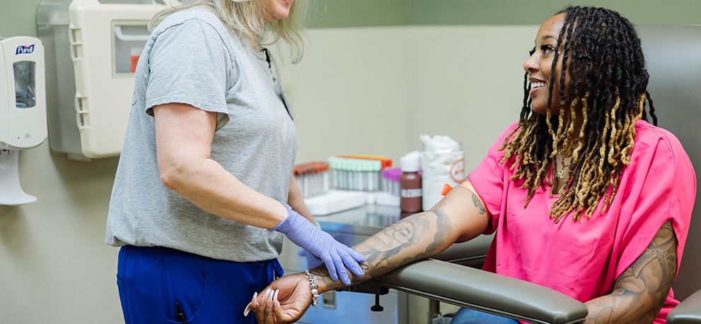 Woman in pink top holding out her arm for a lab tech to take blood
