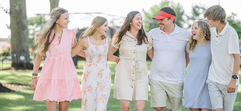 Family with three teenage daughters and a teenage son walking arm-in-arm with mom and dad