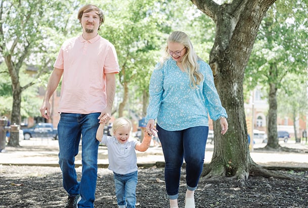 Father and mother holding hands and walking in park with toddler son