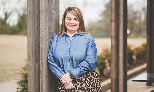 Katy McCully leaning against a column in a blue shirt and cheetah skirt
