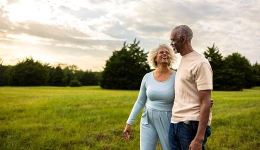 Husband and wife walk through a meadow.