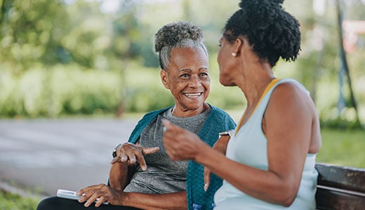 An older woman and middle aged woman chatting on a park bench