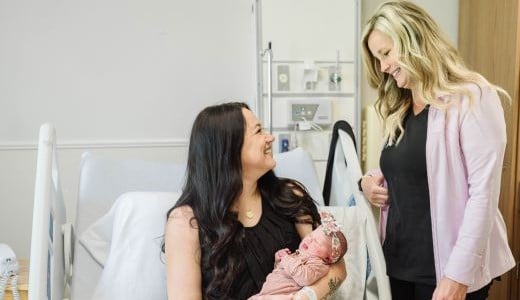 postpartum nurse at Women's Hospital assisting new mother who is holding her newborn daughter