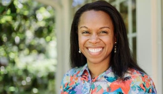 female in bright floral shirt outside large windows, smiling