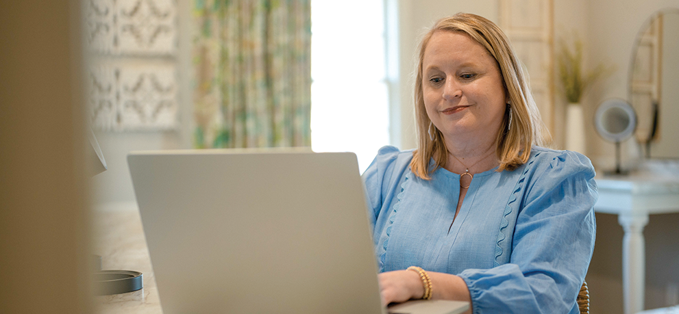 A blonde woman in a light blue top typing on a laptop