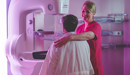 Technologist assists robe-draped woman with mammogram with kind smile