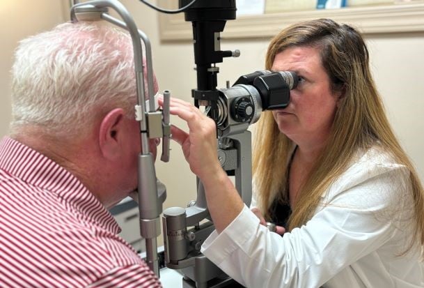 Retina surgeon Dr. Heather Hancock examining a male patient's eye while looking through an instrument in the clinic 