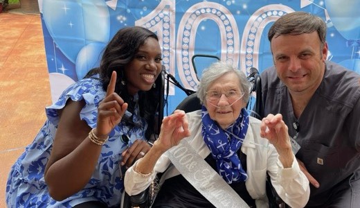 A nursing home resident celebrates her 100th birthday with two staff members.