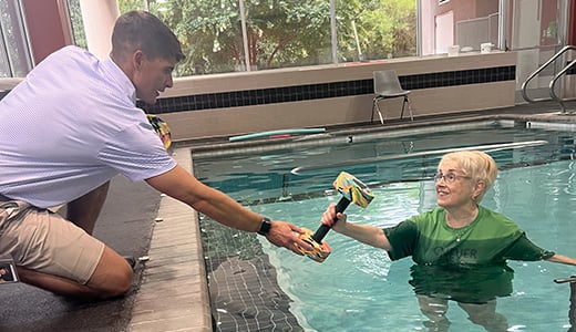 Therapist hands a weight to a woman in the pool during her aquatic therapy session