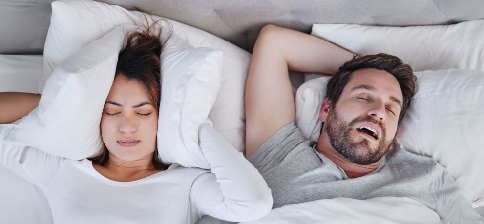 Woman holding pillow over ears to drown out husband's snoring