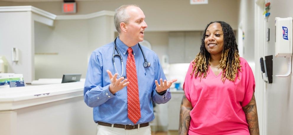 Lady with pink top and a doctor with blue shirt walking in clinic setting near counter