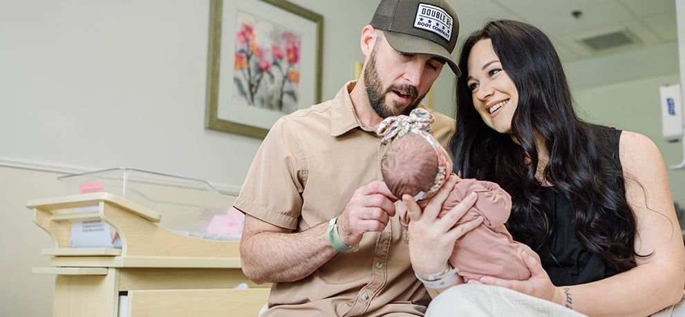 A mother and father hold their newborn on a hospital bed