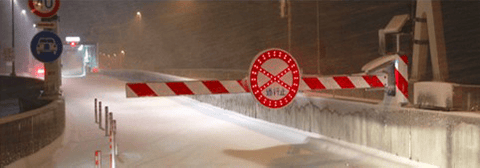 雪が積もる道路に下ろされた赤と白の縞模様の遮断機。中央には、赤いランプで囲まれた『通行止』の丸い標識が取り付けられている。
