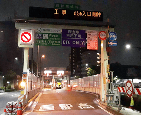 上部の文字情報板には「工事のため入口閉鎖中」と表示され、左側の柱には「車両通行止め」の標識が明るく点灯している。