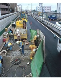 車線規制された高架道路上で、作業員がノージョイント化工事を進めている作業風景の写真