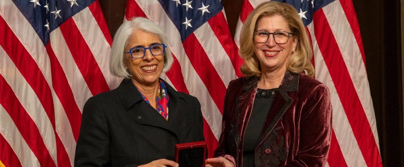 Teresa Woodruff accepts the National Medal of Science award in front of American flags.