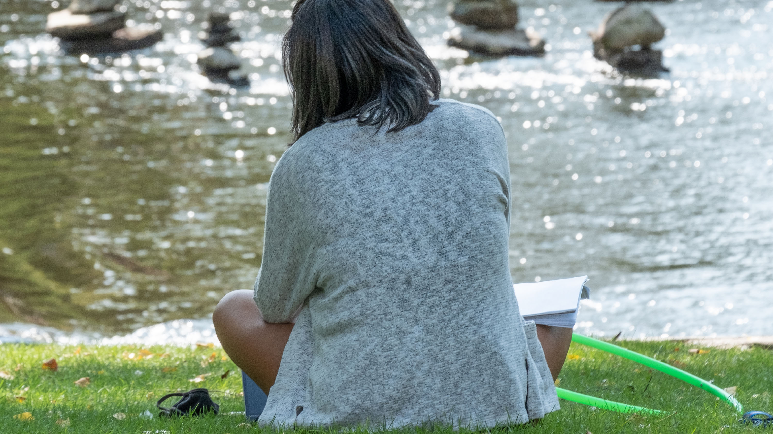 A student studying next to the Red Cedar river.