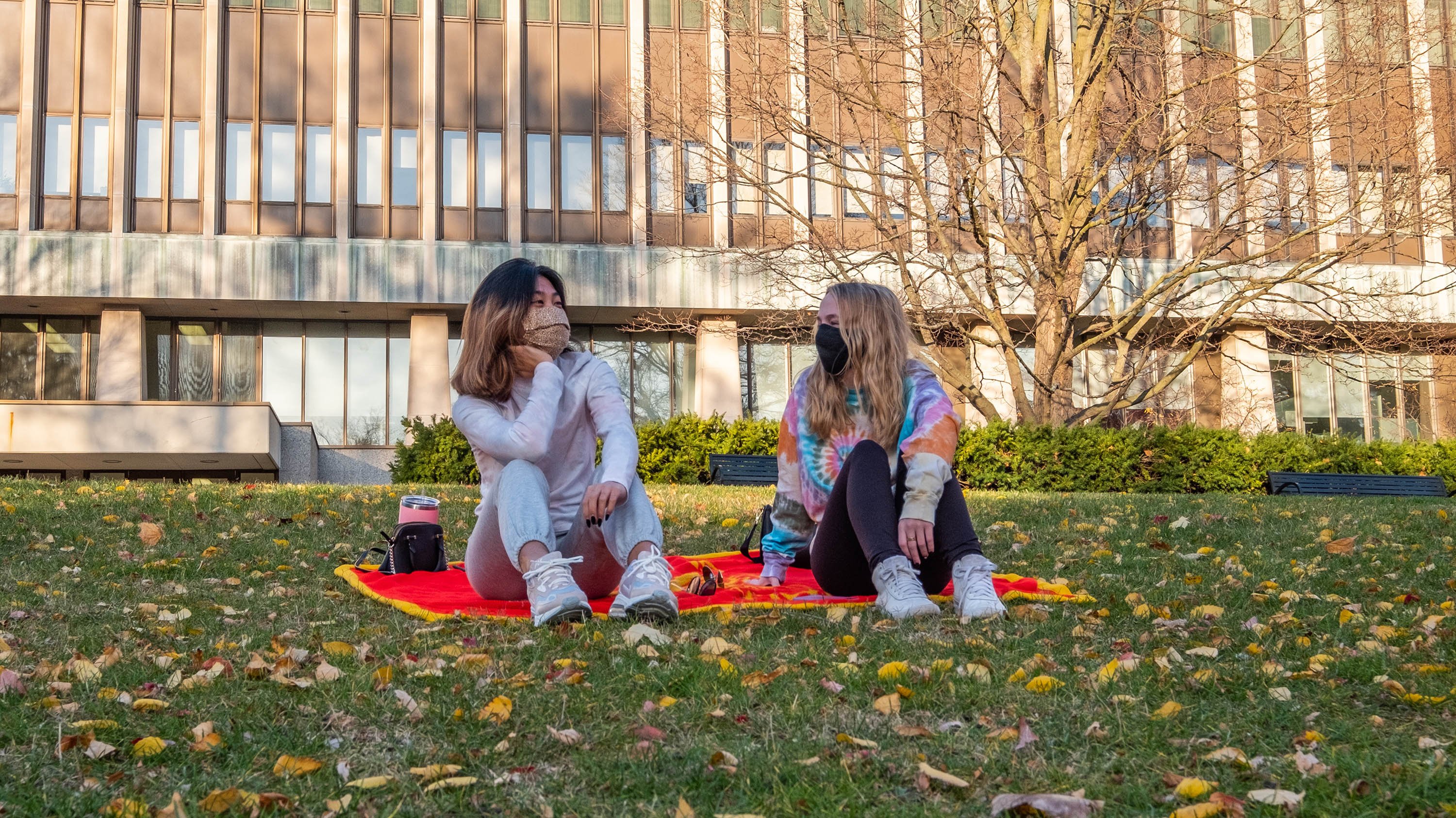 Two students sitting in the grass in front of admin