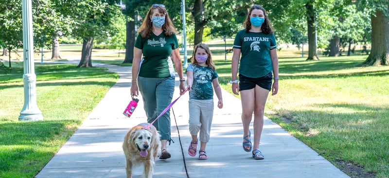 family wearing masks walking with a dog