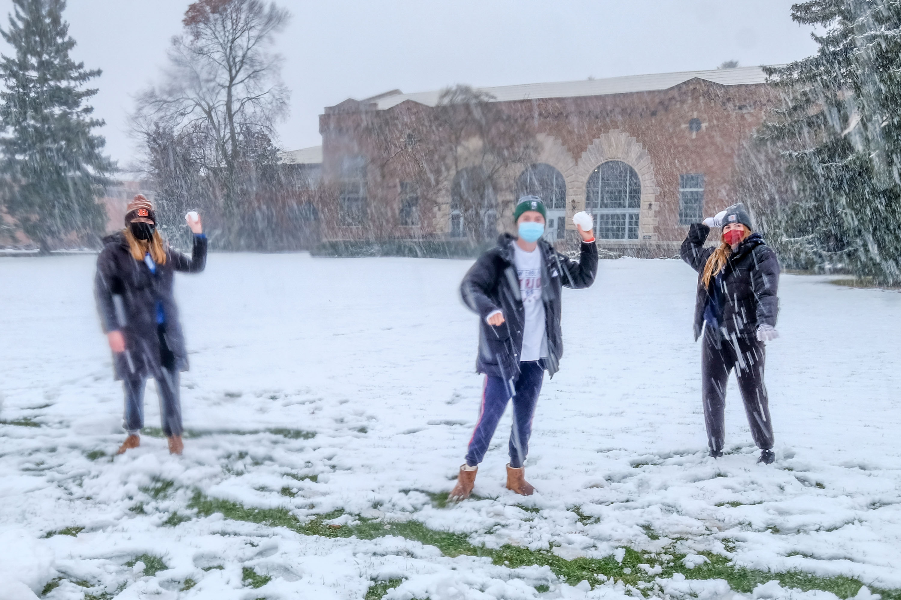 Three female students in Dem Hall Field throwing snowballs.