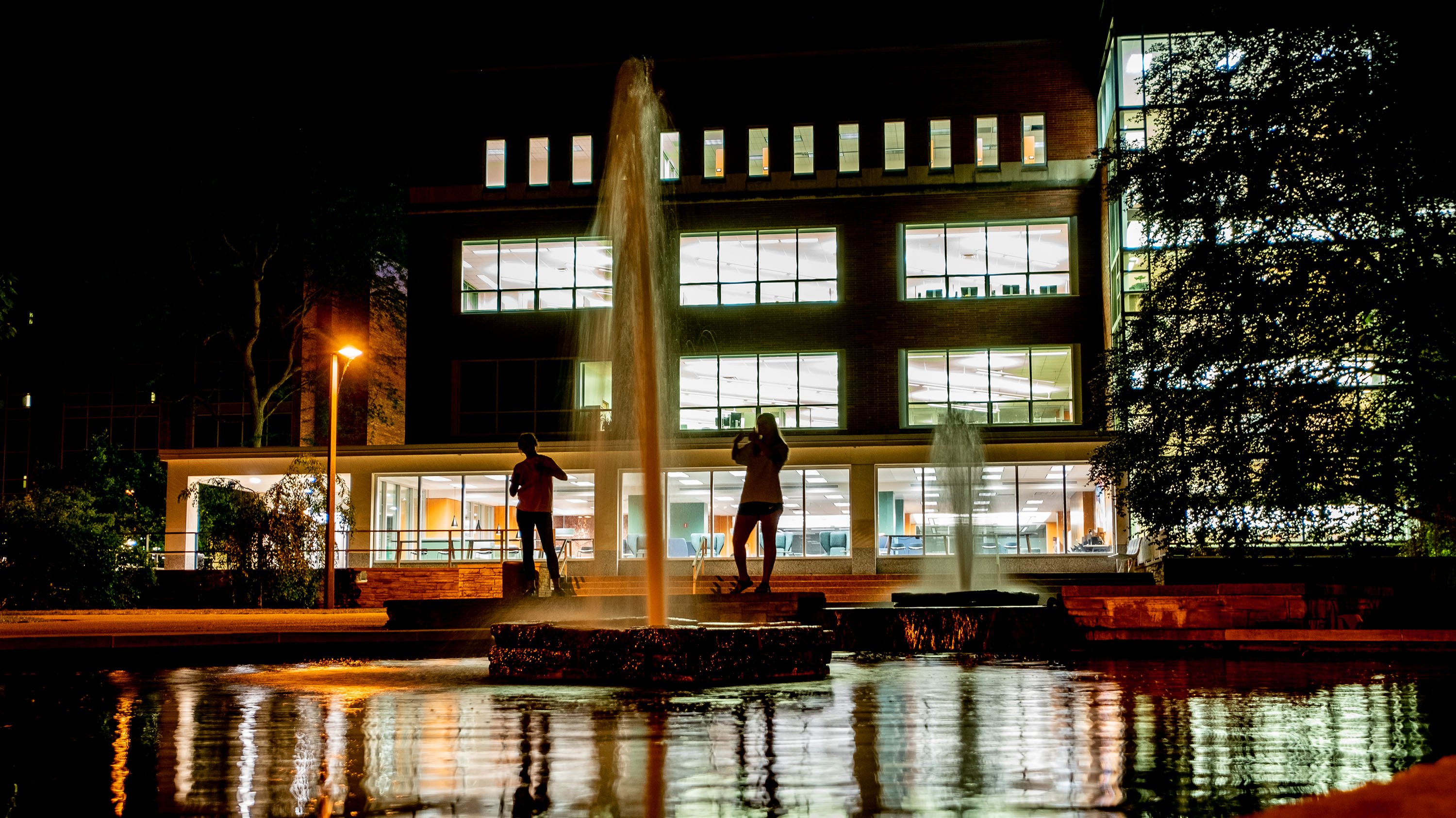 Students standing behind the Library Fountain at night