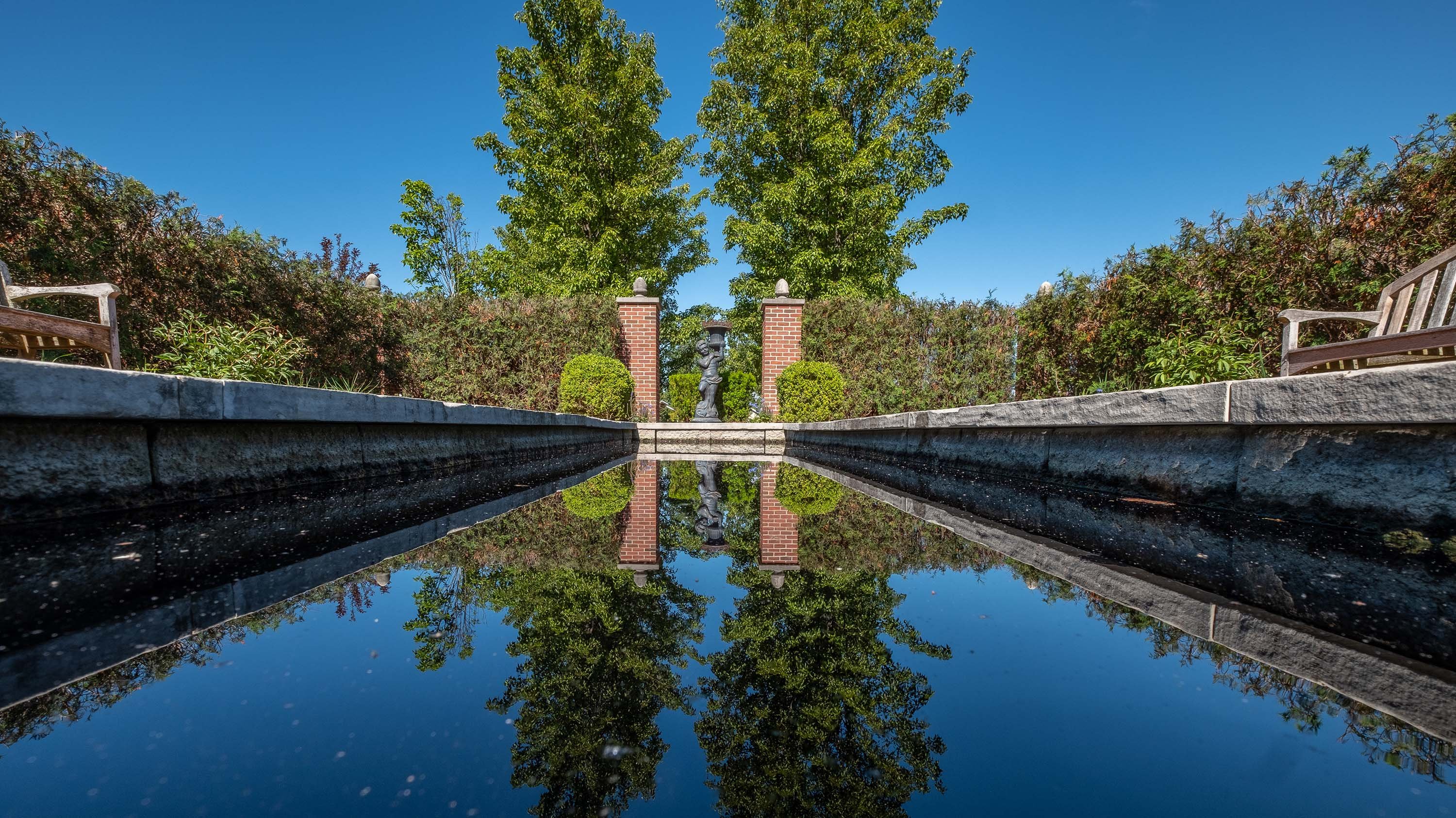 A pond in the Webb English garden, reflecting the garden and a sculpture in the water