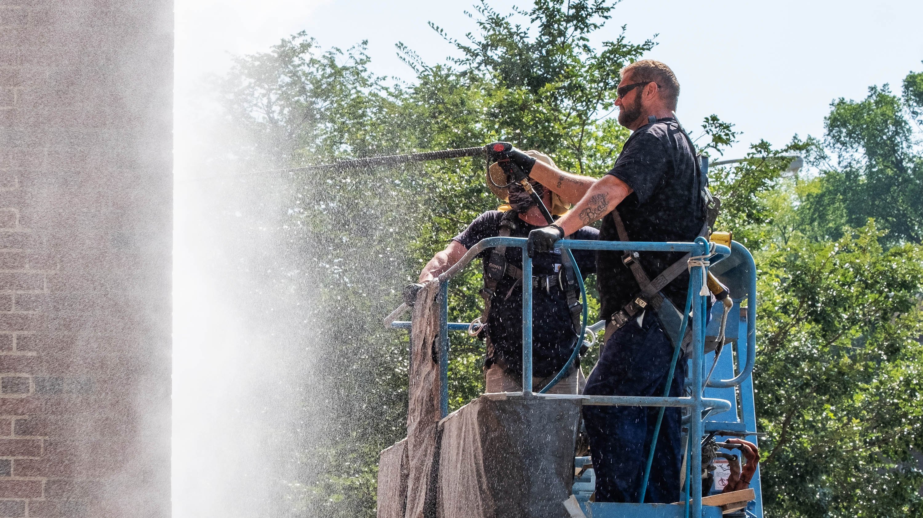 Two IPF crew members using a power-washer on one of the exterior walls of South Kedzie Hall