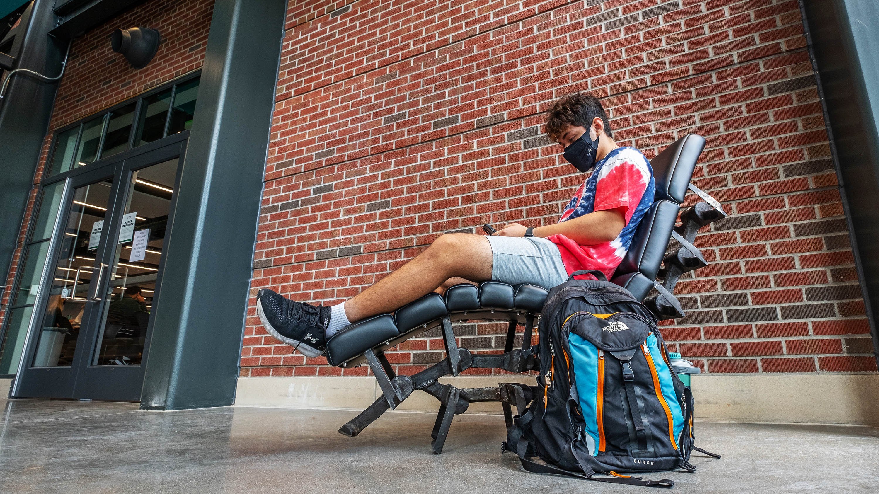 Student sit in a chair in the new STEM building.  The chair frame is made out of conveyor belt in the old Power Plant.