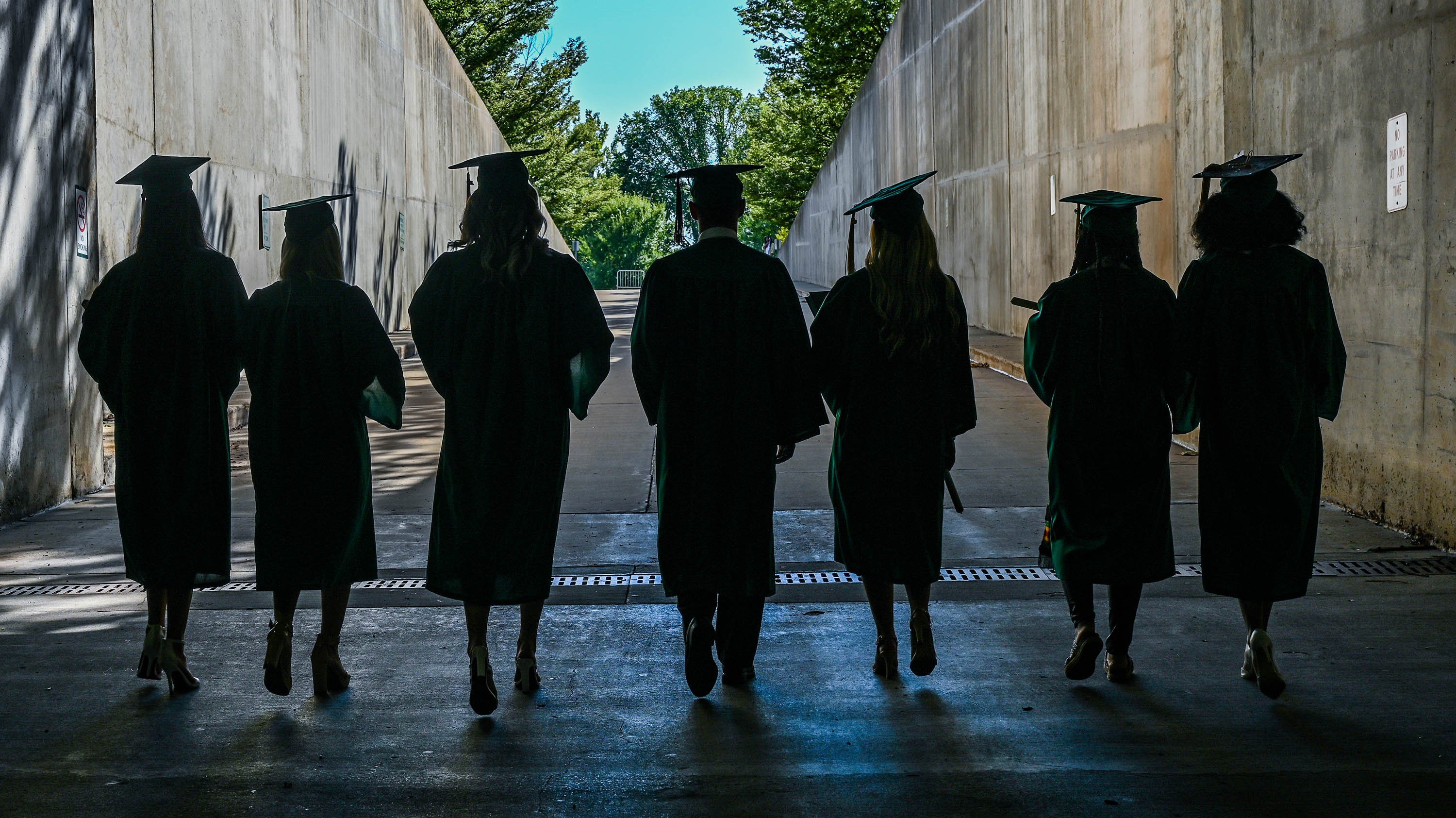 MSU graduates in caps and gowns, walking out of Breslin Center tunnel after graduation