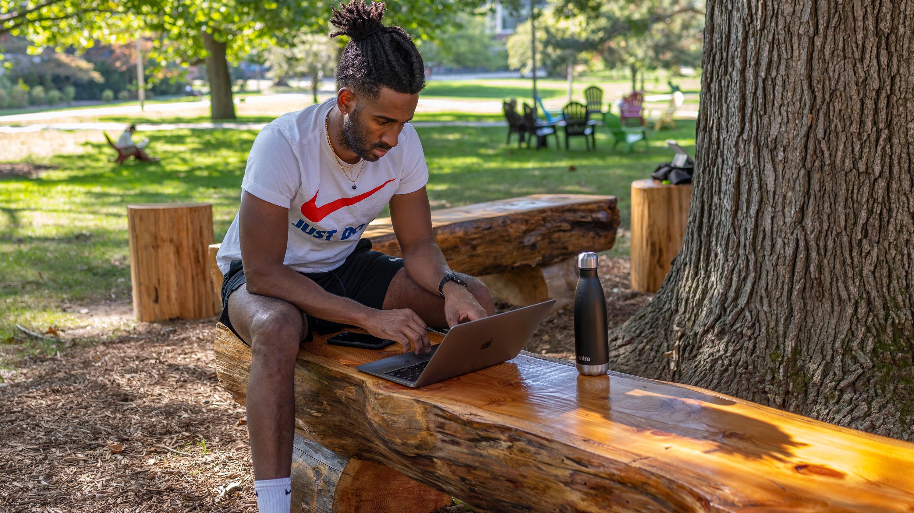 Student using laptop while sitting on reclaimed wood bench