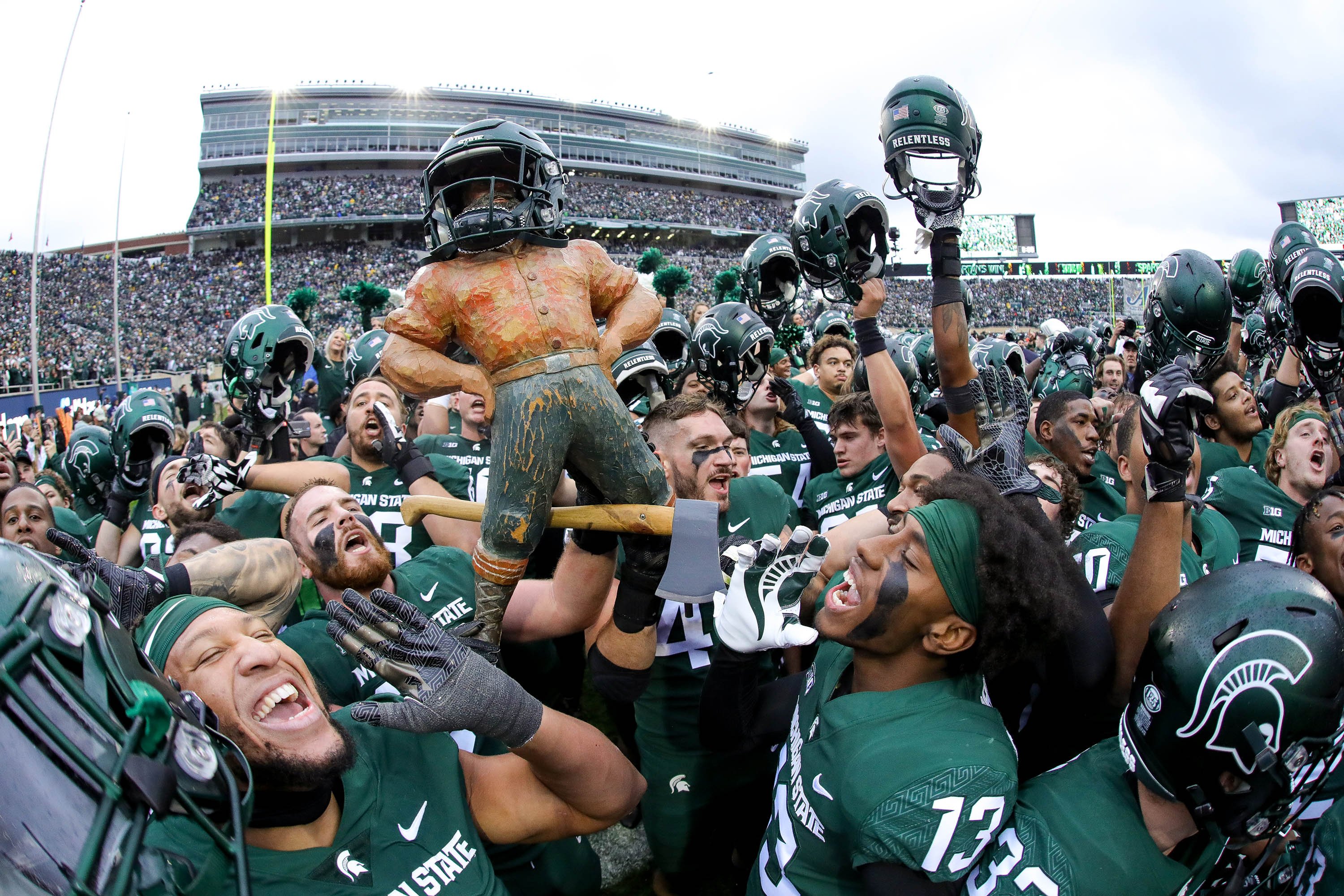 Spartan football players celebrating with the Paul Bunyan trophy