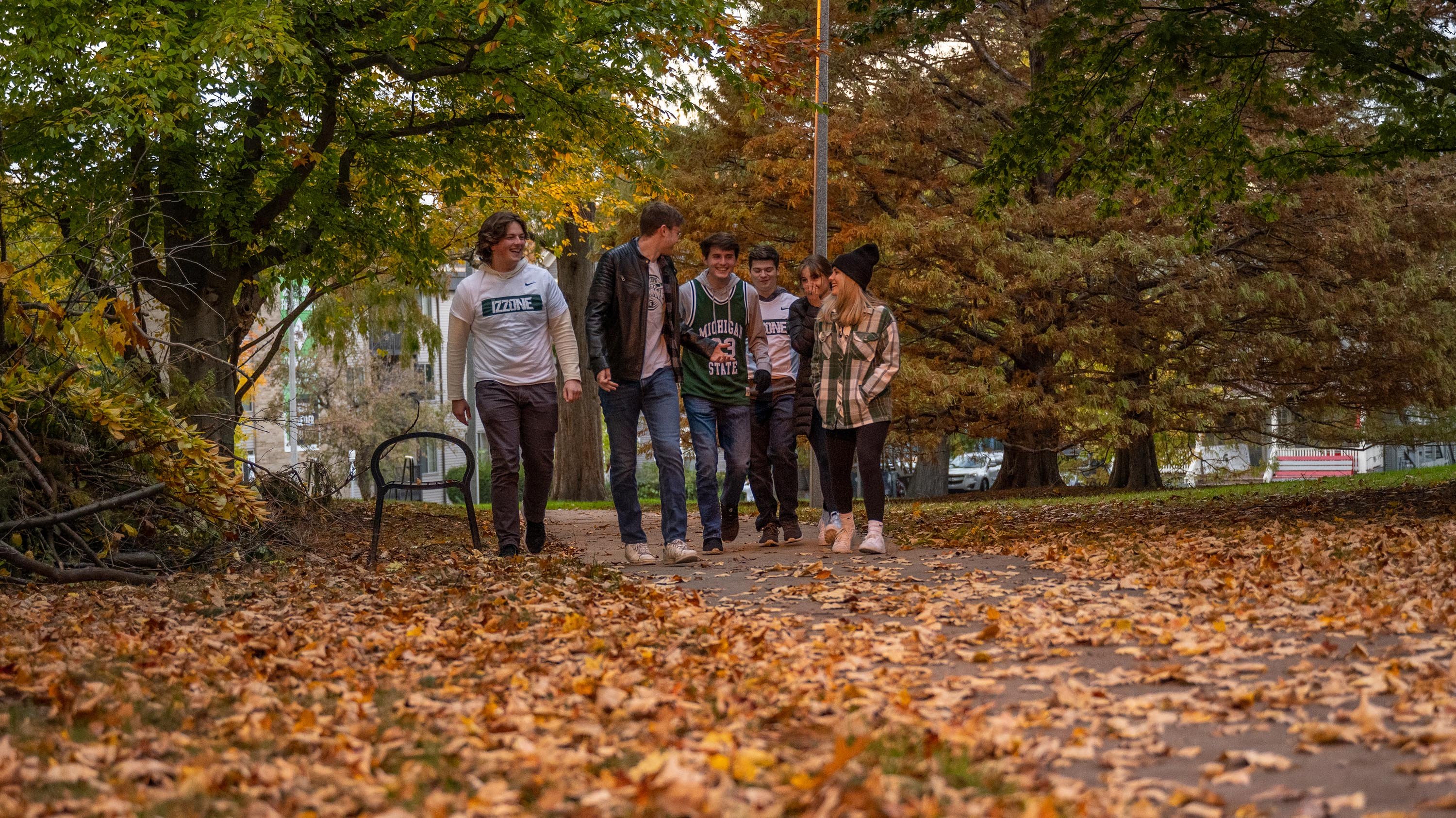 A group of students in Izzone shirts and basketball jerseys walking on campus on a fall day