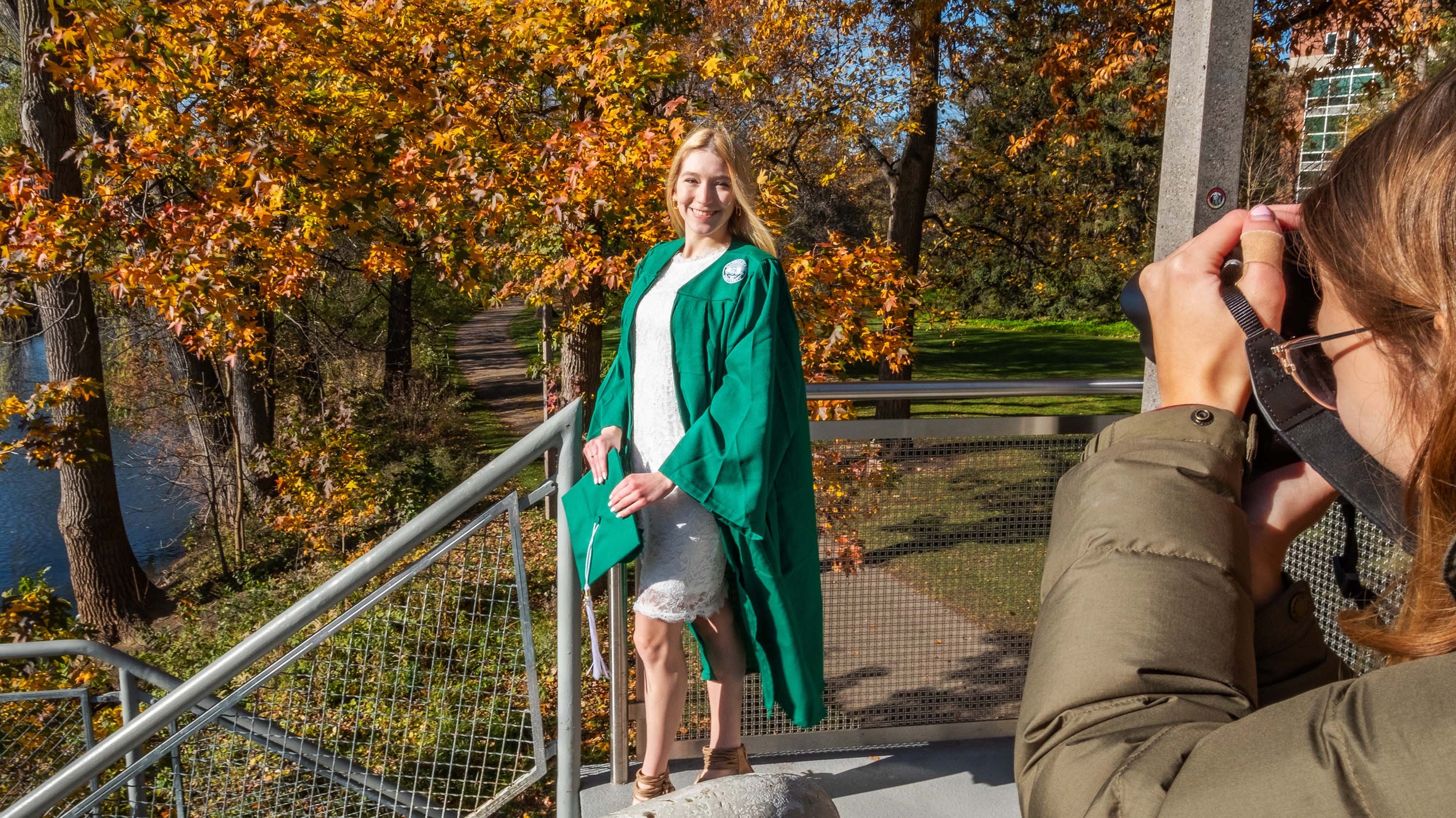 Photographer taking picture of student in cap and gown on library bridge