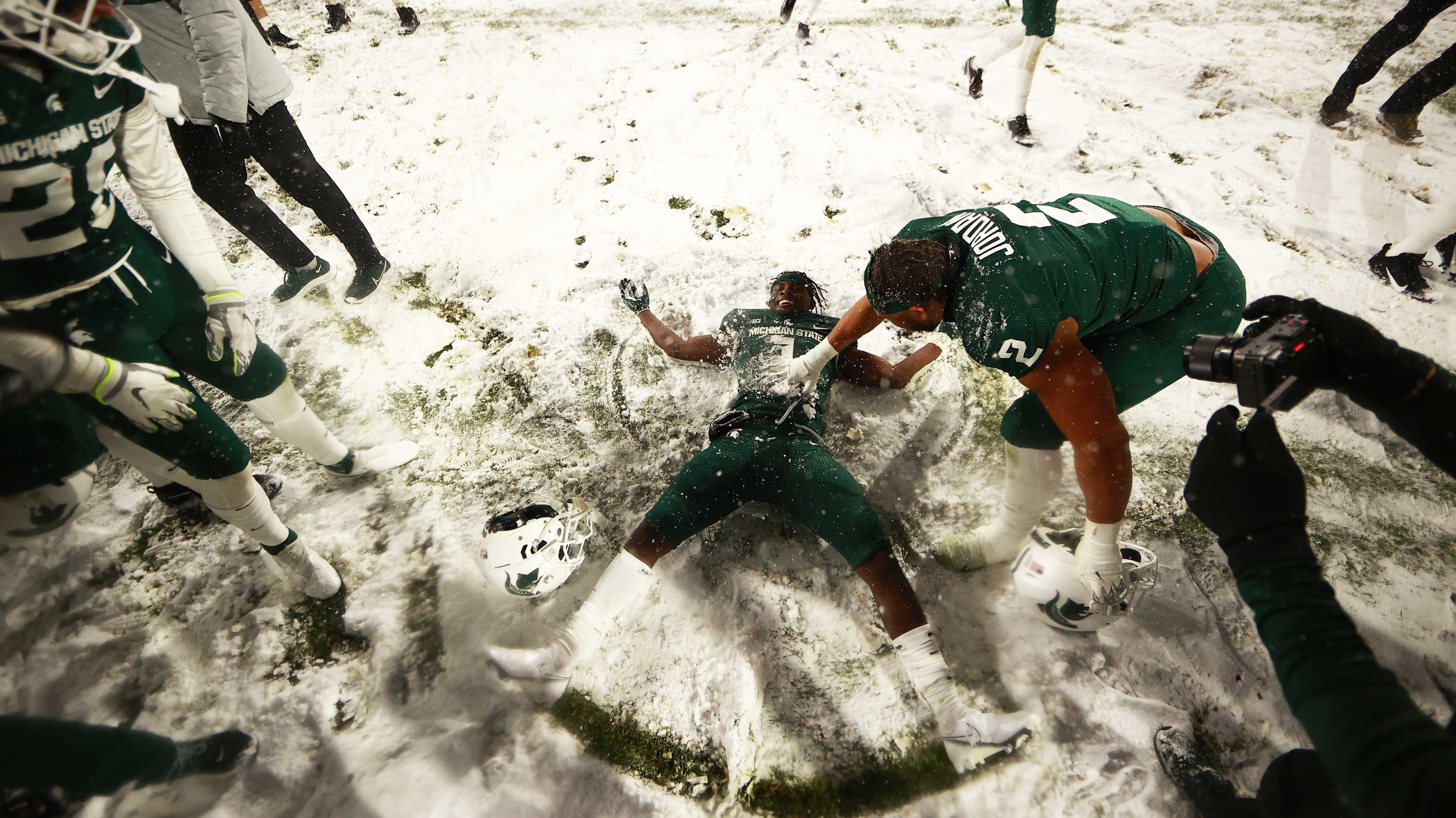 MSU football player making a snow angel in Spartan Stadium after game