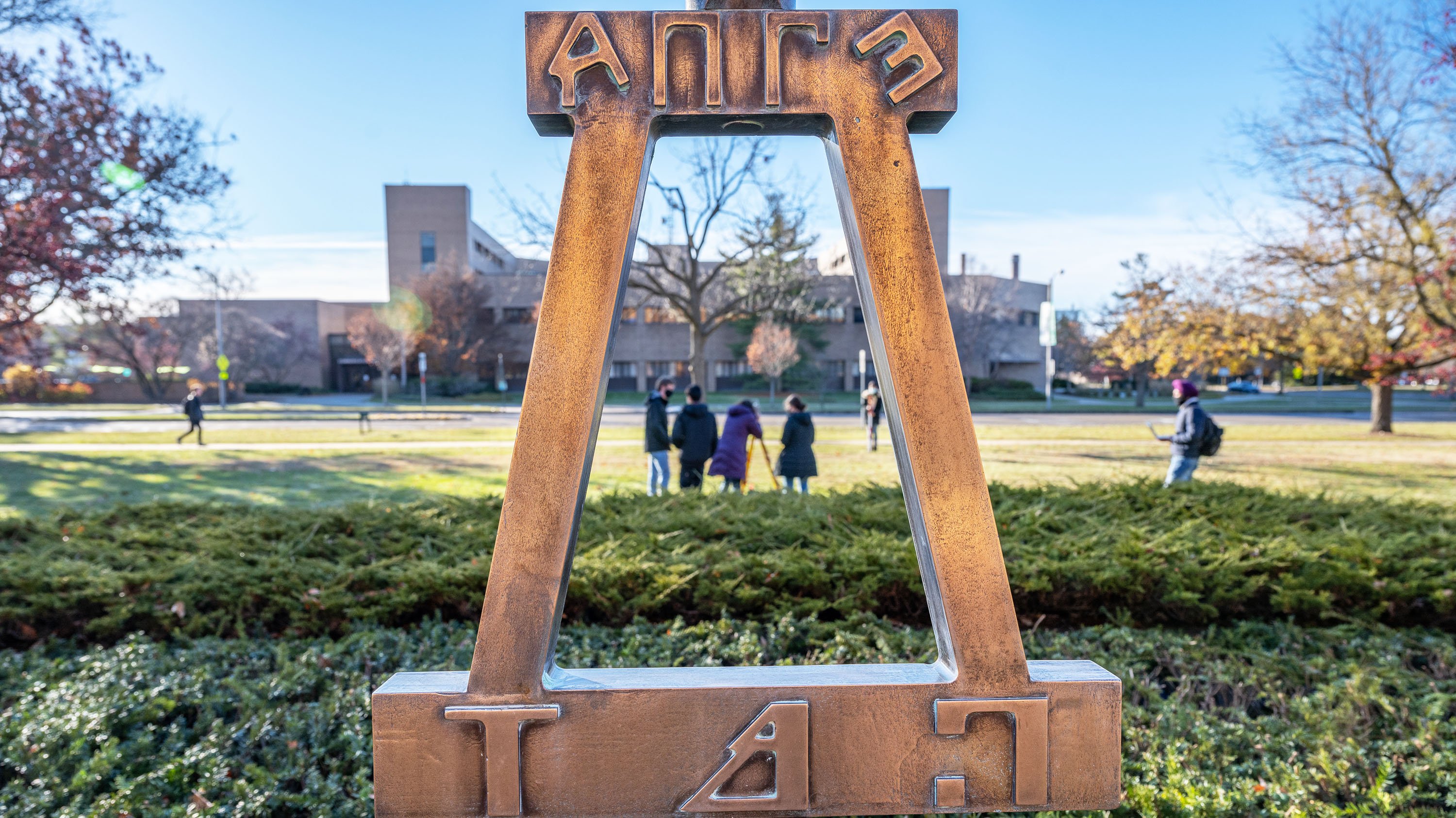 Engineering students taking their final exam outside of the Engineering Building, as seen through the sculpture outside the building
