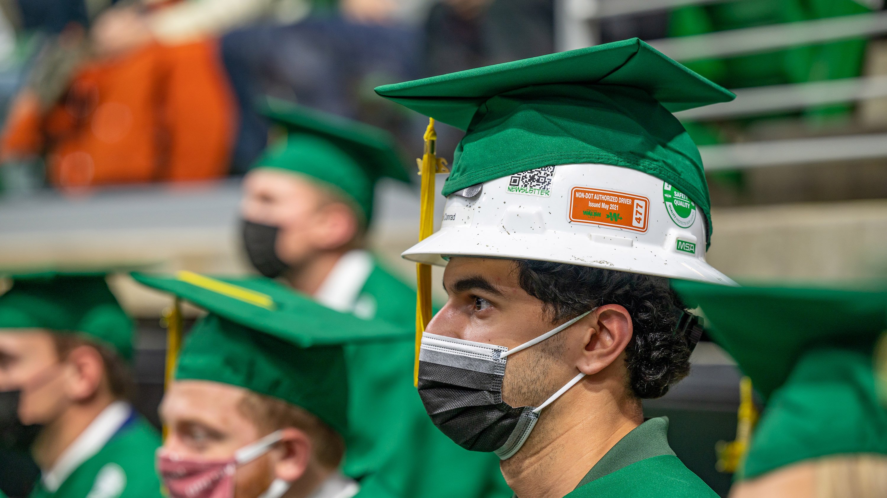 Graduate at commencement ceremony wearing construction helmet under his grad cap