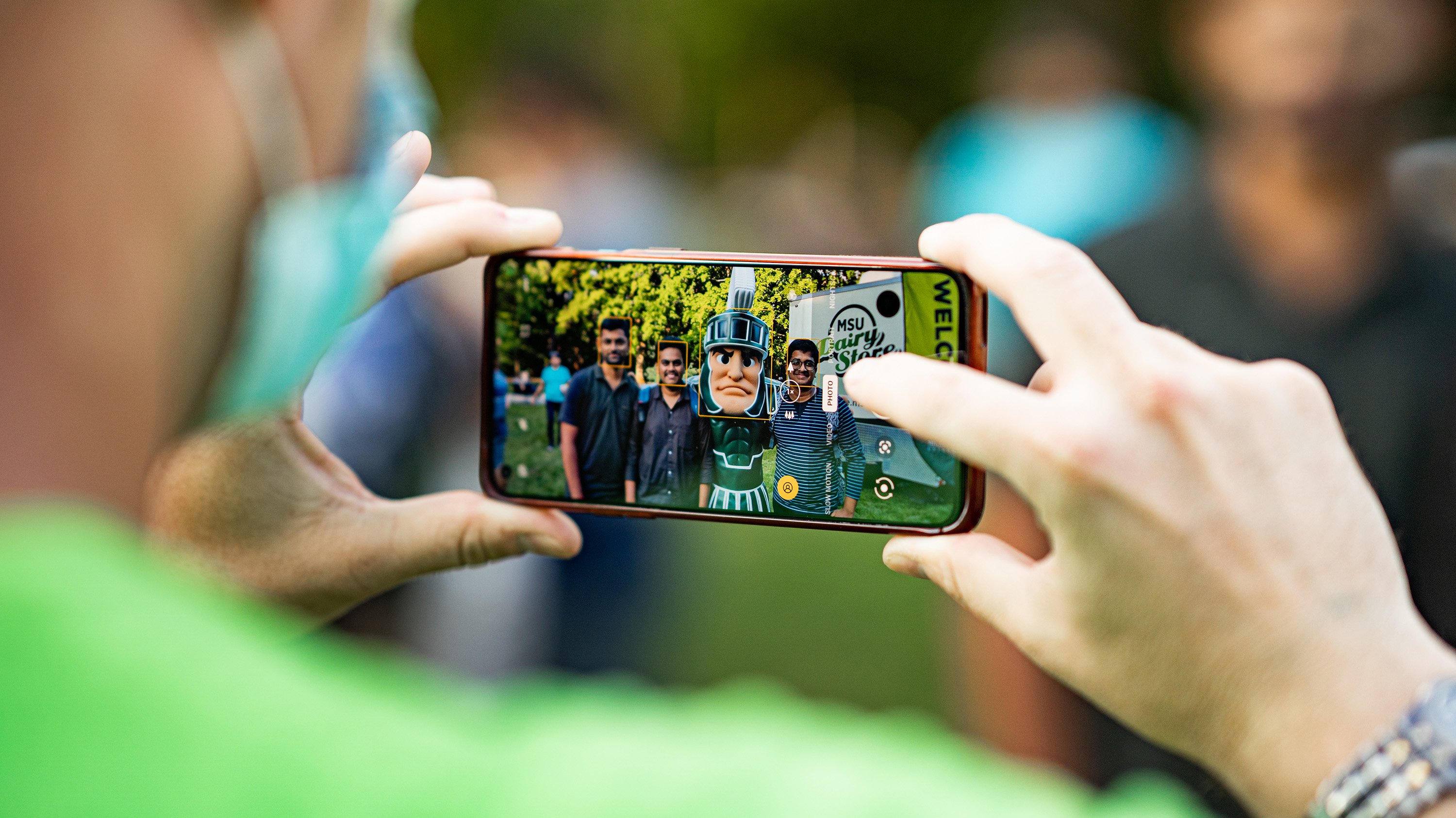 Person holding phone showing a photo with Sparty and students