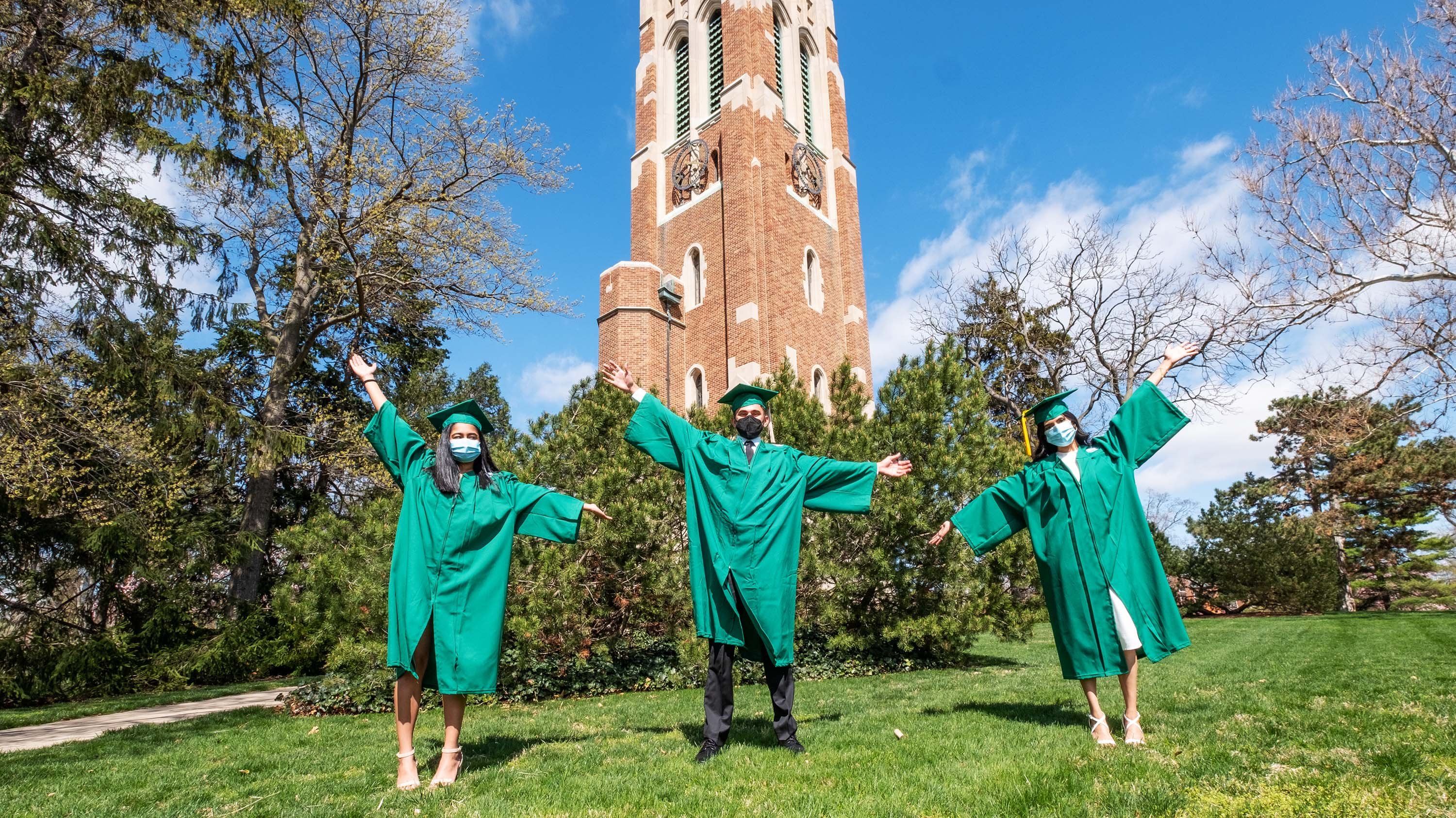 Three students in graduation gowns posing in front of Beaumont Tower