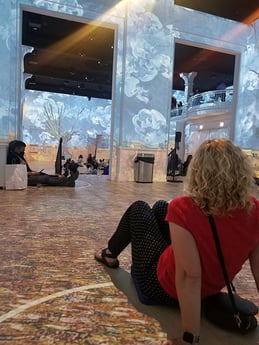 Lisa sitting on floor looking at paintings illuminated on the wall and floor