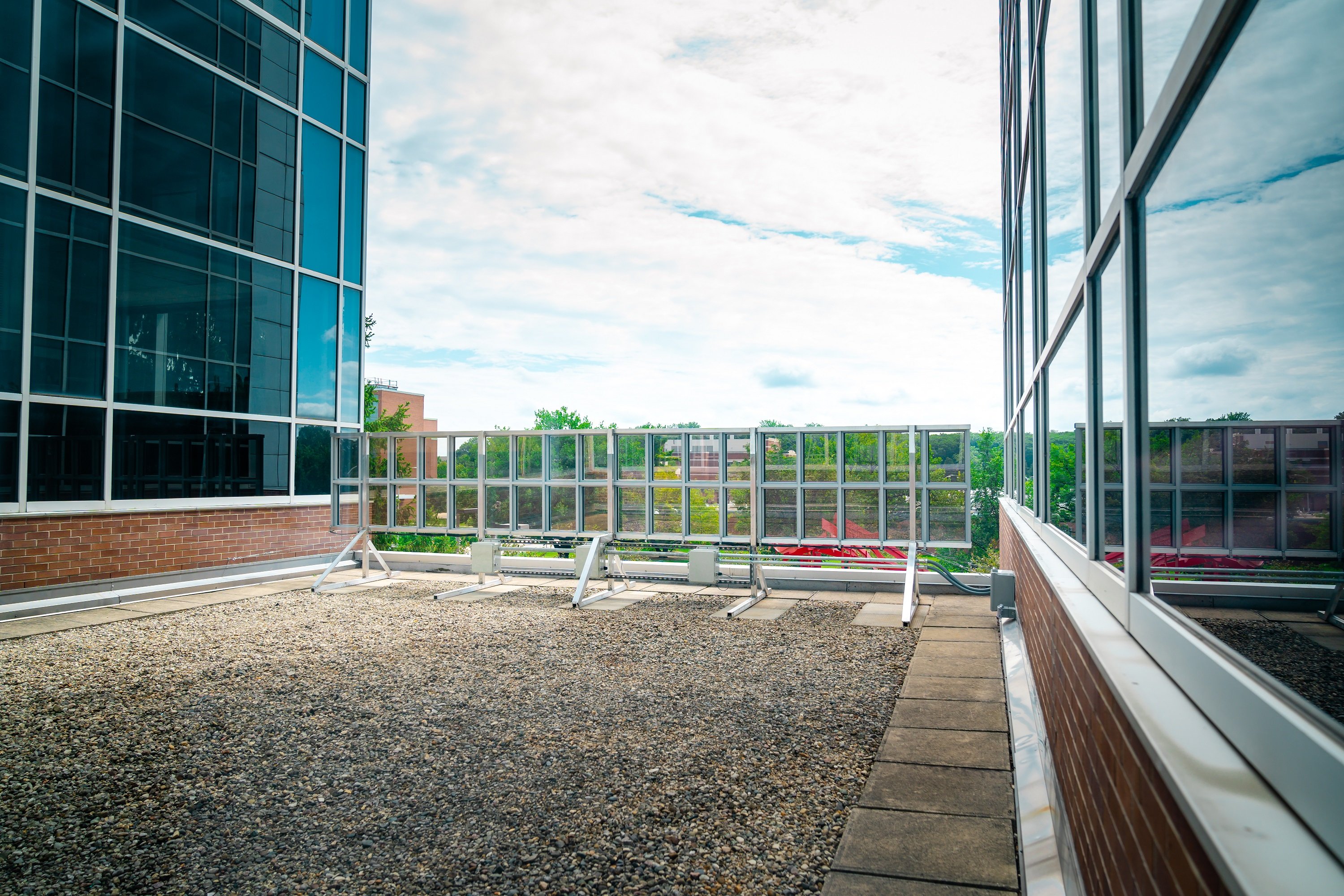 Walls on the right and left of the image with an area covered in gravel in between. At the end of the gravel is a structure with a grid of glass panels against a cloudy sky.  