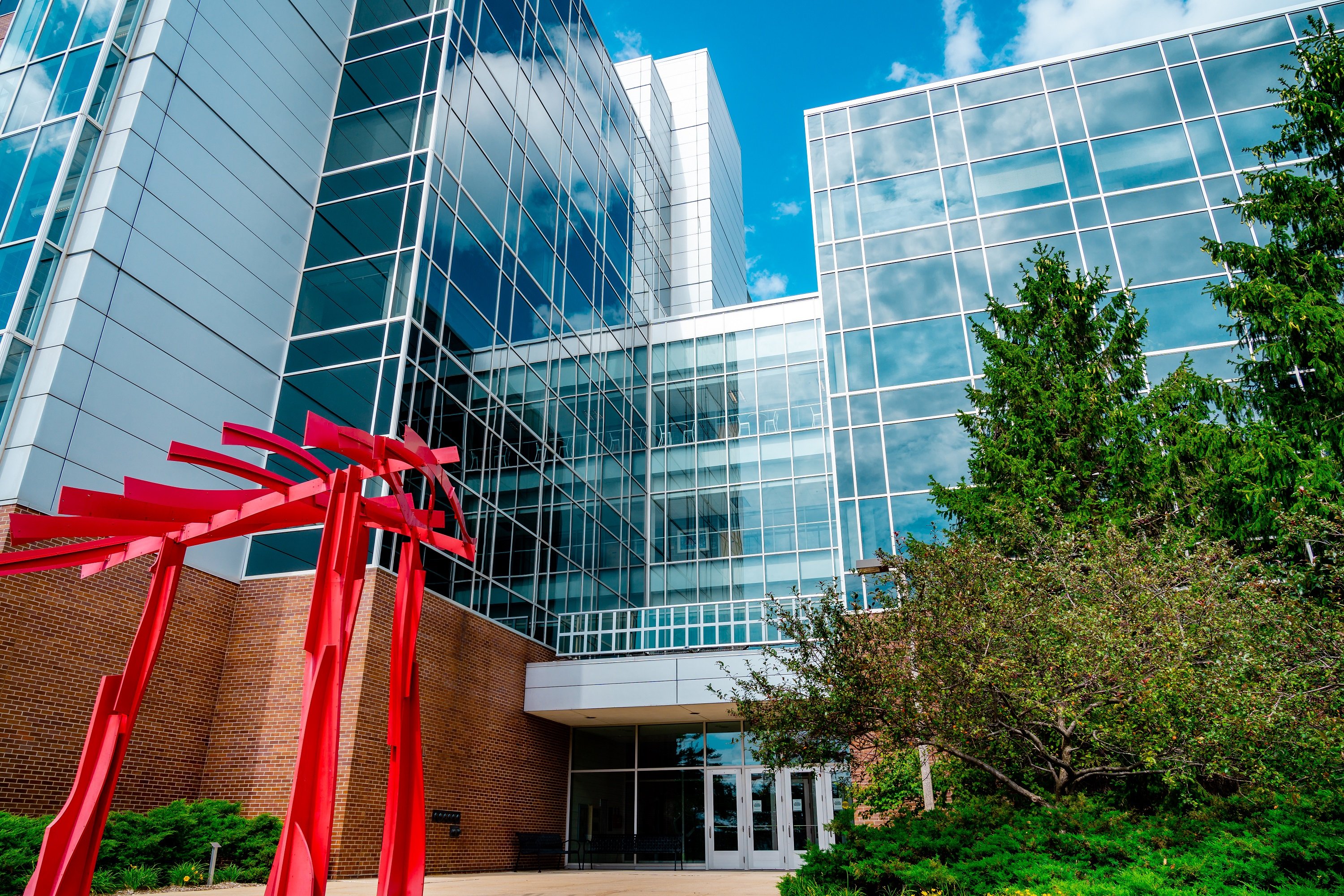 The front of the Biomedical and Physical Sciences Building with green trees and a red sculpture. 