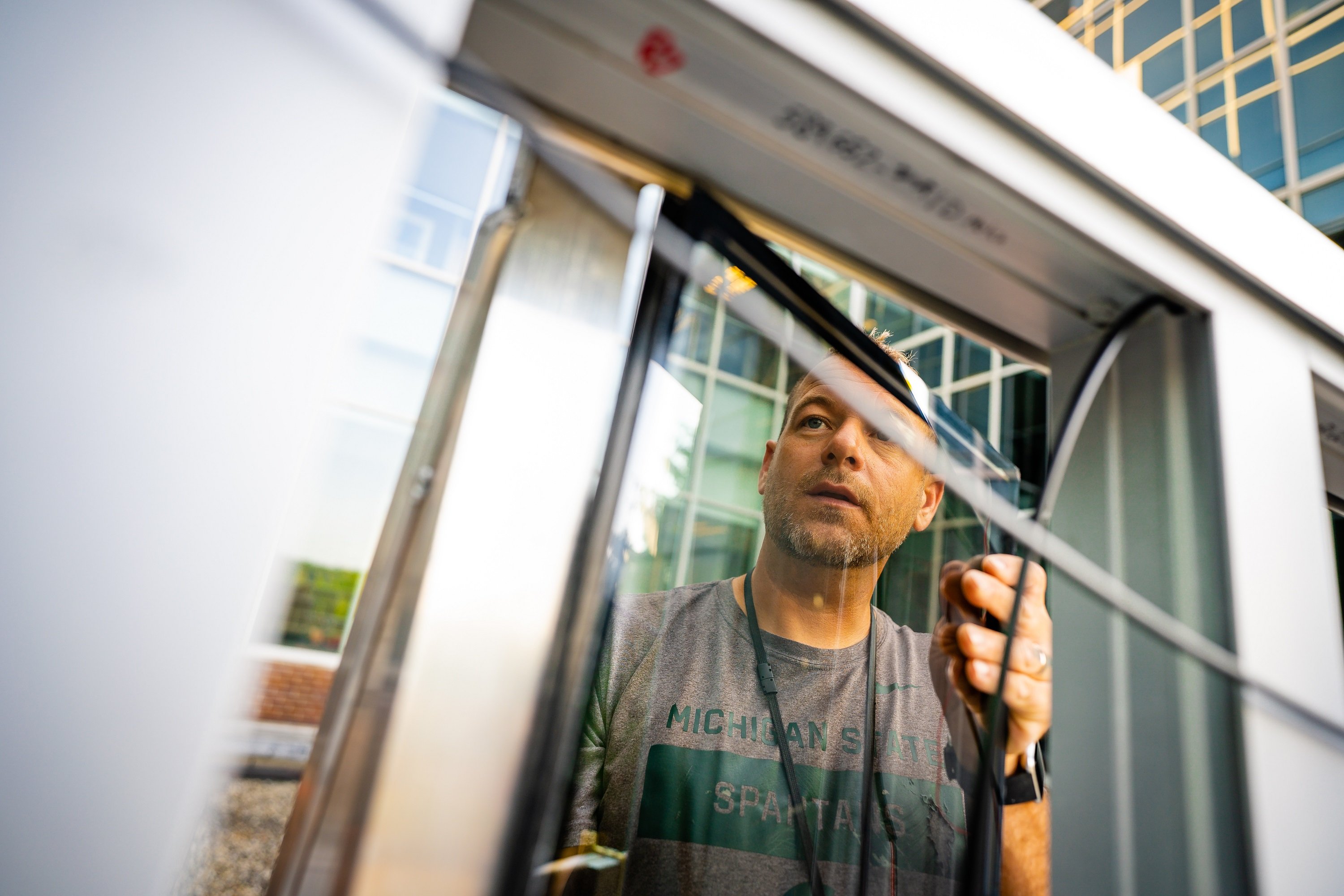 White male in a gray MSU t-shirt fits a piece of glass into a metal grid. 