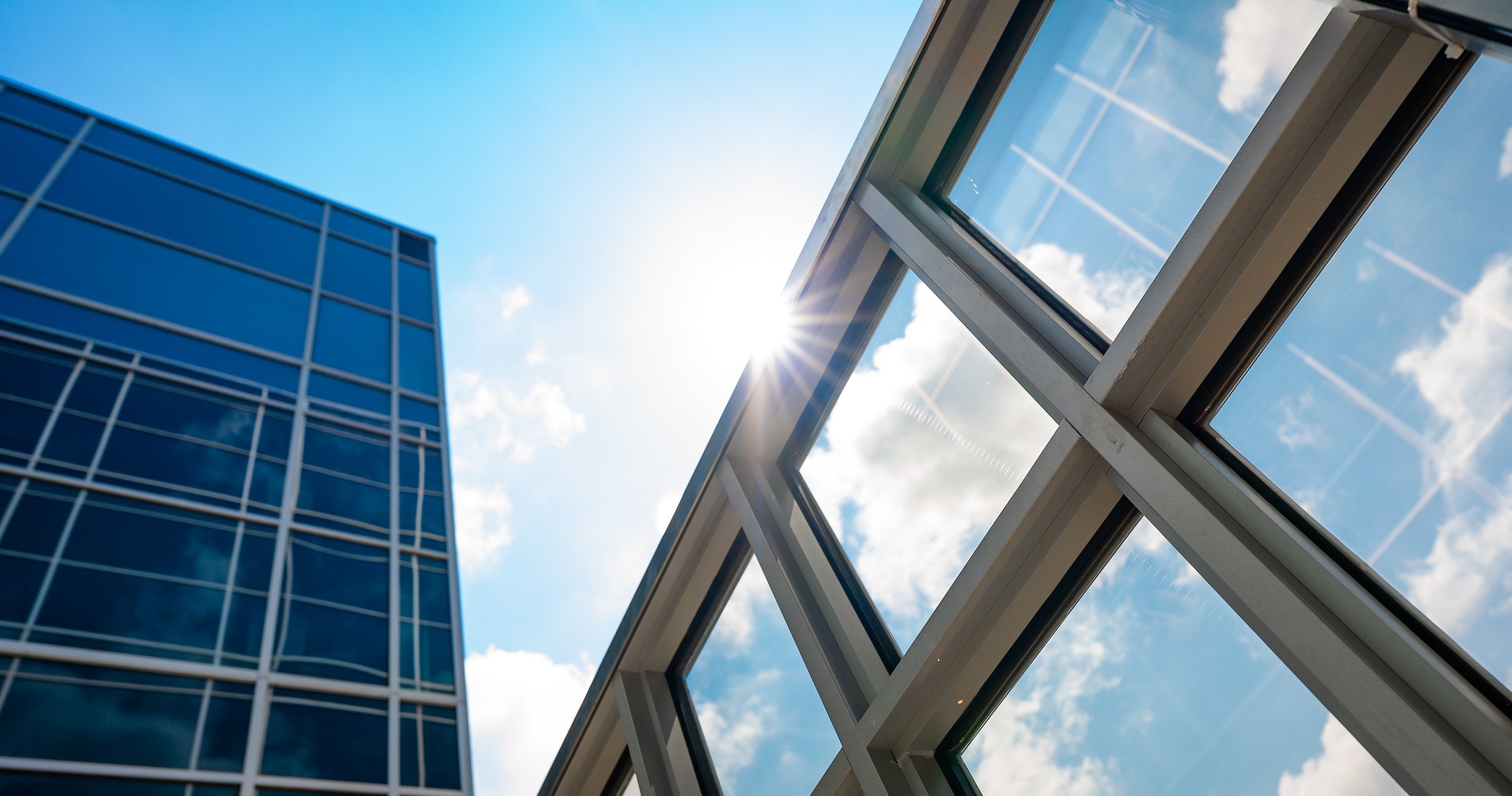 A metal grid of windows against a blue sky with a burst of sun. 