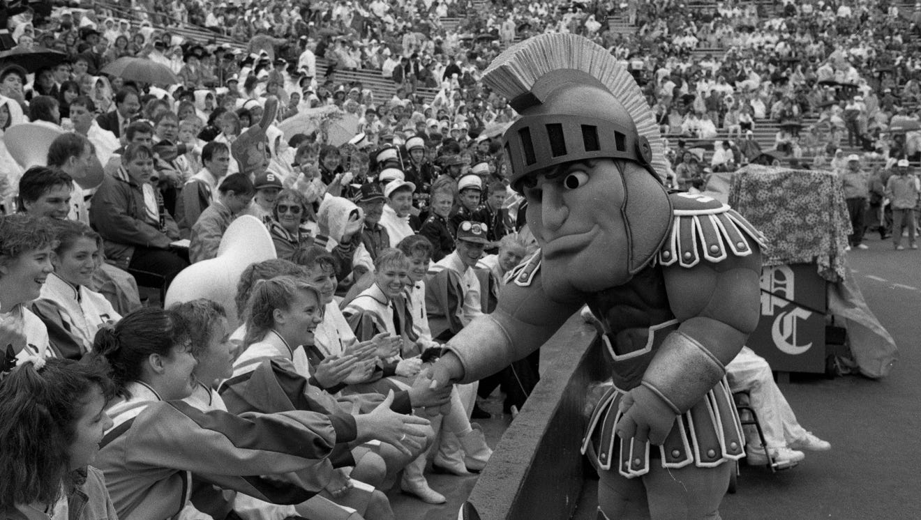 Black and white photo of Sparty greeting the crowd at a football game, 1989