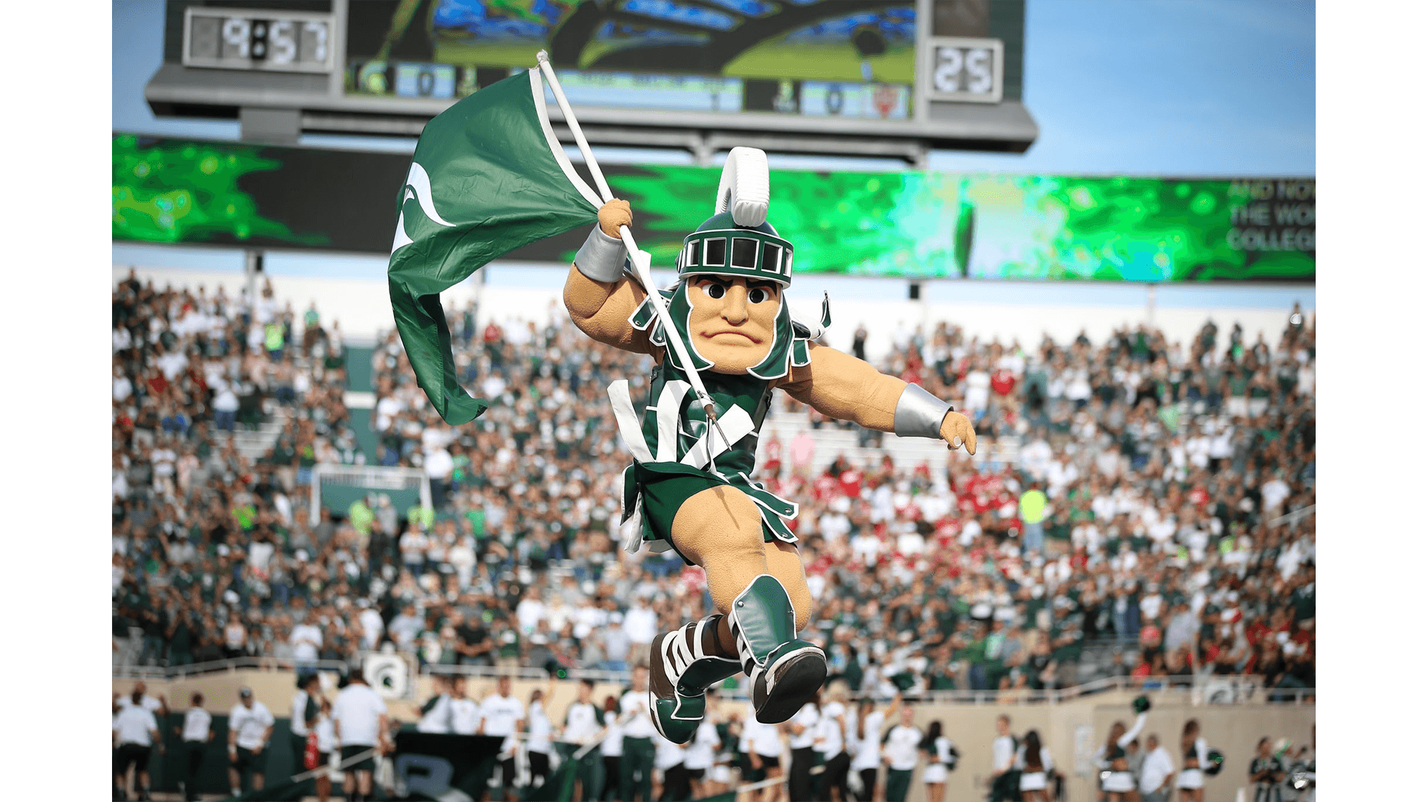 Sparty holding a flag and jumping in the air during a football game