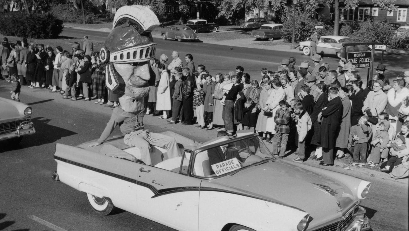 Old version of the Sparty mascot riding in a convertible during a homecoming parade, 1955