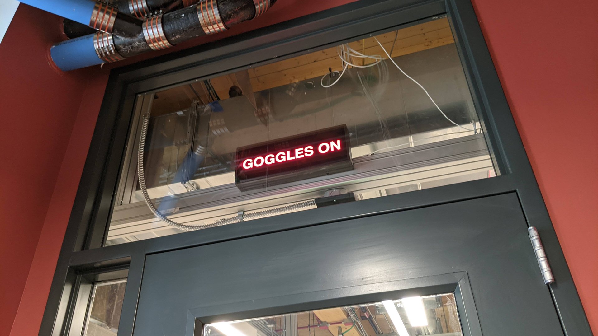 A photograph shows a lighted sign above a door to a chemistry lab that says 'Goggles on.'