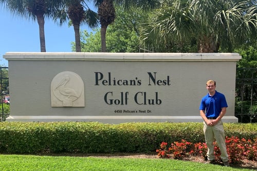 student Jackson Severns in front of Pelicans Nest Golf Club sign